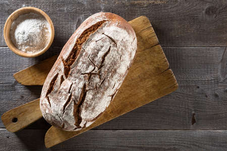 Freshly baked bread with cup of flour and cutting board on Rustic wooden table; Top view