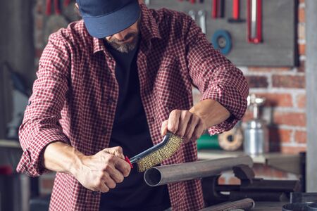 Metalworker using a hand metal brush on a metal pipe inside an engineering workshop