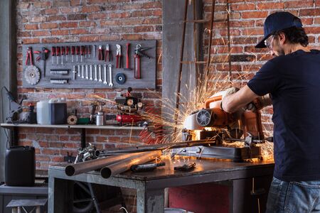 Metalworker grinding or cutting metal in a shower of sparks while working at his workbench on a pipe in a factory or engineering workshopの写真素材