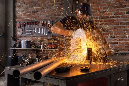 Man doing metalwork in a workshop using a grinding wheel with flying fiery sparks against a backdrop...