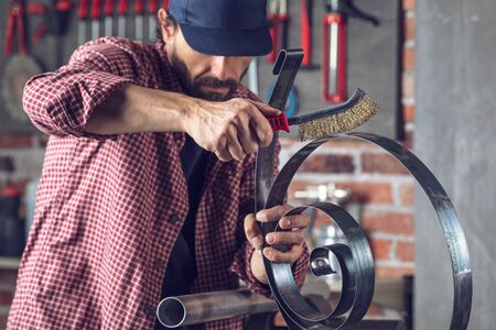 Metalworker using a hand metal brush on a metal object inside an engineering workshopの写真素材