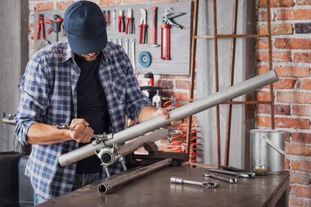 Metalworker tightening a bolt or clamp with a spanner as he joins two metal pipes together in an engineering workshopの写真素材