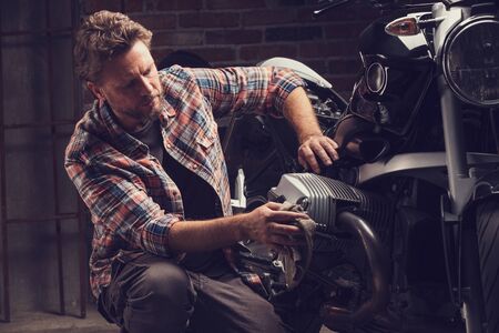 Collector or mechanic working on the engine of a vintage motorcycle in a shadowy workshop in a close up viewの写真素材