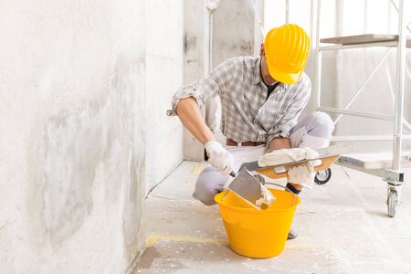 Plasterer loading new plaster from a bucket using a trowel to repair a wall of a house with damp stains from moisture or a leakの写真素材