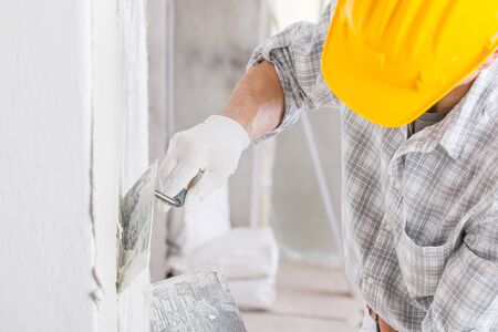 Builder using a trowel to add plaster to a white wall during repairs for a damp area caused by water leakage or moistureの写真素材