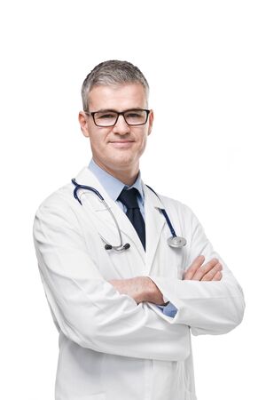 Confident male doctor in white lab coat, eyeglasses and stethoscope standing with folded arms smiling at the camera isolated on white