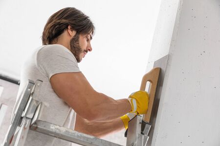 Plasterer finishing the surface of a white wall using a trowel during building or renovations on a house interiorの写真素材