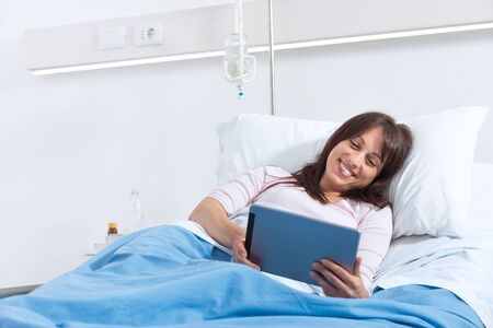 Young smiling patient lying in a hospital bed and she is watching video with digital tabletの写真素材