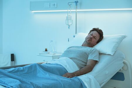 Adult man lying in a hospital bed at night and sleepingの写真素材