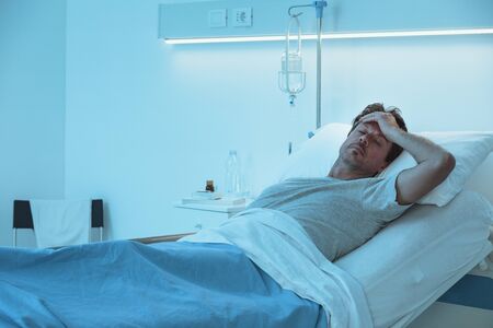 Adult man lying in a hospital bed at night and he is sufferingの写真素材