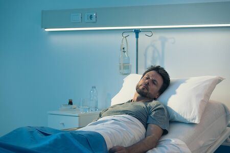 Adult man lying in a hospital bed at night and sleepingの写真素材