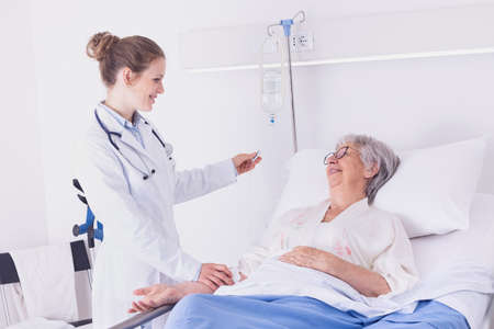 Nurse or doctor checking a drip on an elderly woman patient lying in a bed on the ward with a warm friendly smile in a healthcare conceptの写真素材