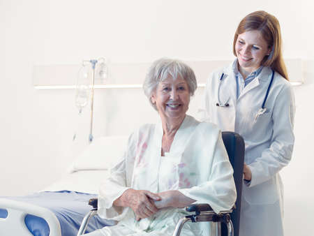 Smiling happy senior woman in a wheelchair in hospital or an old-age home being wheeled by a doctor or nurse during rehabilitation from an injury or surgeryの写真素材