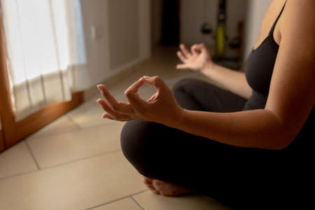 Meditation at home. Young attractive woman in lotus position in front of the window. Relaxation and atmosphere conceptの写真素材