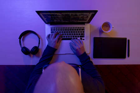 Top view of photographer, videographer or designer sitting at desk and works on his laptop from home on a wooden desk. Blue light . High quality photoの写真素材
