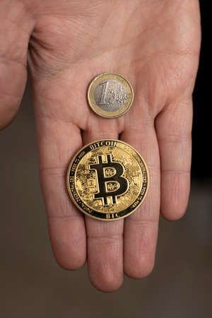 Caucasian hand shows one Bitcoin coin and one Euro Coin. New finance concept. Comparison between currencies, fiat and crypto. One handの写真素材