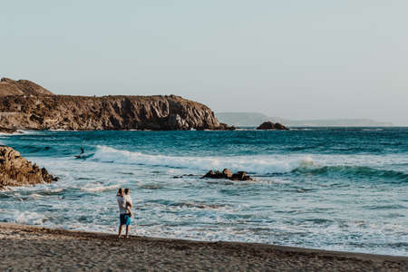 A man with his son at the beach looking surfersの写真素材