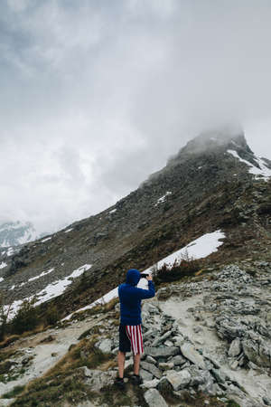 Hiker with short pant American Flag Taking photo with his smart phone to the panorama in the mountainの写真素材
