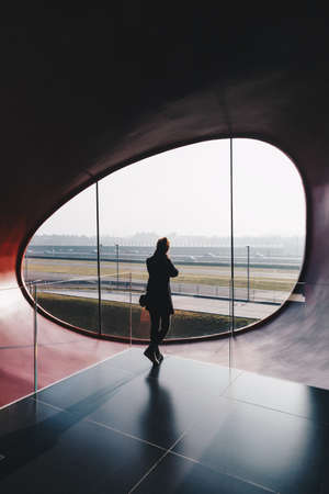 woman standing in a futuristic and modern office building, looking outside - oval modern windowの写真素材