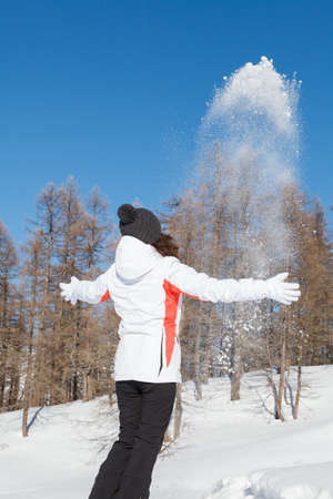 Girl dispersing snow in the air and having fun outdoors on winter day with blue ski and trees on the backgroundの写真素材