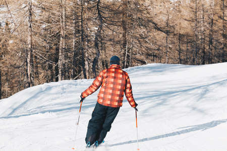 Skier skiing with checked jacket down the slope in the forest - Downhill in high mountains.