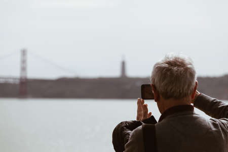 Senior Man taking picture with smart phone at the bridge in Lisbon - Portugalの写真素材