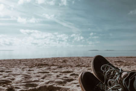 trekking shoes in the foreground - people taking rest at the beach in a sunny dayの写真素材
