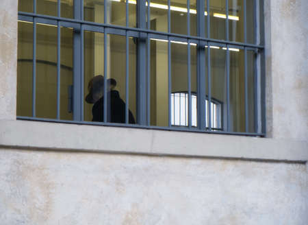 sad old senior man with hat inside building with barred windows - Law and justice concept
