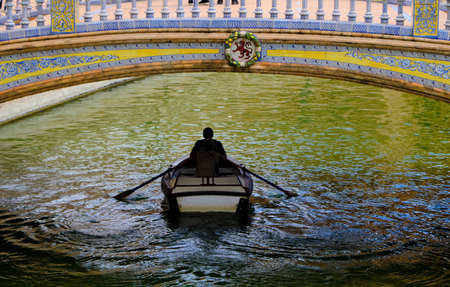 lovers on the little boat under the bridge of Andalisia Seville's main square Plaza de Espana.