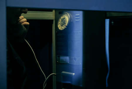 woman hand talking in a old vintage telephone cabin at night urban 80s mood