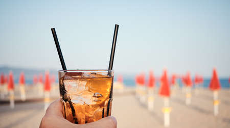 hand close-up holding Colorful glass cocktail at sunset at the beach with seascape blurred backgroundの写真素材
