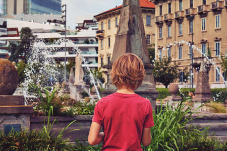 young boy with red t-shirt looking at fountain in Milan - solitude conceptの写真素材