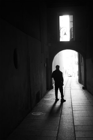 Silhouette of a person in a narrow alley, illuminated by exterior light, creating a mysterious, contrasting black and white scene.の写真素材