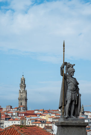 statue of a warrior holding a spear, standing atop a pedestal, with a church tower visible in the background against a blue sky with clouds. in the city of Porto in Portugalの写真素材
