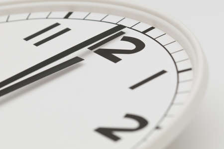 White clock with black hands showing one minute to midnight, noon