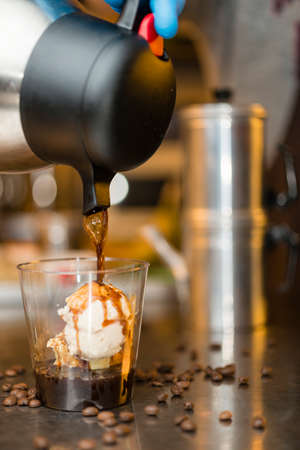 Artisan preparation of a glass cup of Italian ice cream gelato affogato, drowned, in espresso coffe with whipped cream and cat's tongue cookies.の写真素材