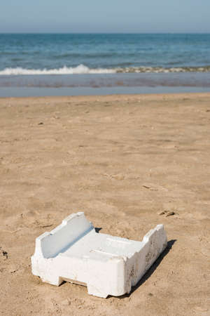 Plastic, white,  container left on sandy beach.の写真素材