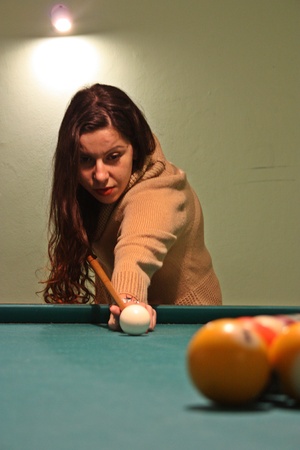 brown-haired caucasian girl plays billiards. the cue, the balls and the holes.