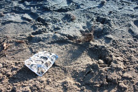 a pack of pills. blister of medicines left on the sandy beach. pollution. plastic left in nature....