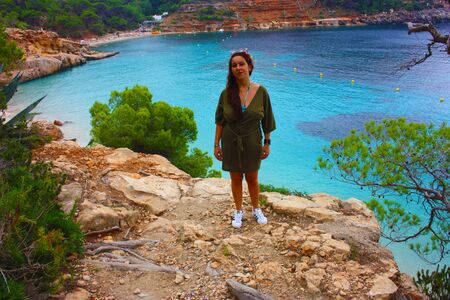 caucasian girl on the cliff of cala saladeta enjoys summer vacation in the wild nature of the balearic islands enjoying in ibizaの写真素材
