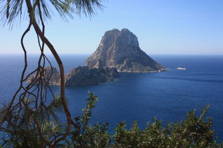 The magical island of Es Vedra with the small islet of Es Vedranell next to it in front of the coast of Cala d'Hort in the tourist island of Ibiza in the midst of nature between cliffs, beaches and coasts in spainの写真素材