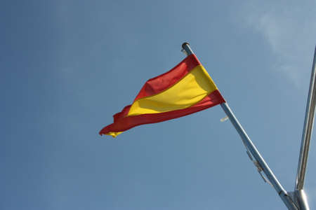 typical Spanish national flag in red and yellow horizontal bands against the skyの写真素材