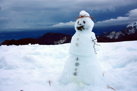 white snowman with twigs and stones and the panorama of the Apuan Alps between mountains and blue...