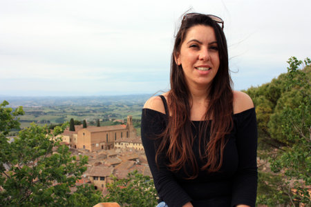 charming brunette caucasian girl and the background of medieval and hilly tuscany of san gimignano in italyの写真素材