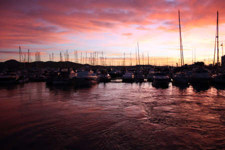 fiery red and purple sunset on ibiza coast view from port at balearic sunset between boatsの写真素材