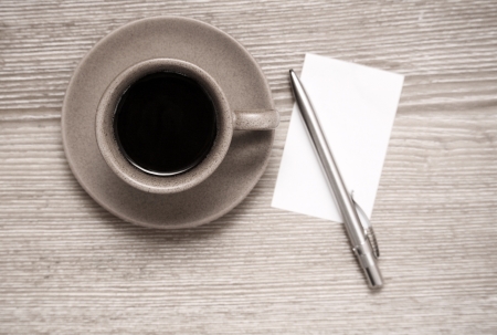 Toned image, cup of black coffee, pen and blank sheet of paper on wooden tableの写真素材