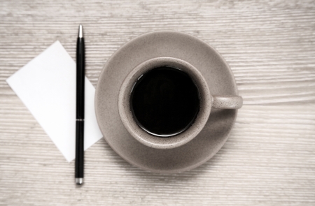Toned image, cup of black coffee, pen and blank sheet of paper on wooden tableの写真素材