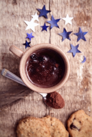 Toned image, hot chocolate, spoon with cocoa, cookies, blue paper stars on a wooden tableの写真素材