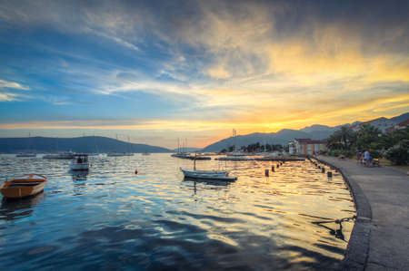 The sky at sunset reflects in the mother-of-pearl water surface, on which lonely boats wander. Order in the Kotor bay contrasting the outlines of the mountains.の写真素材