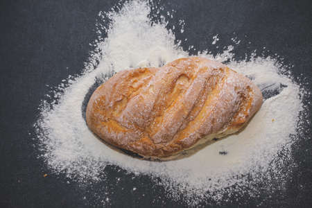 A loaf of white bread on dark kraft paper, powdered with flour.